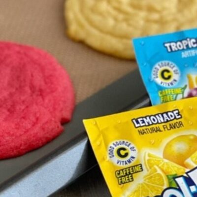 Fresh baked Kool-Aid cookies on a pan with two packets of drink mix.