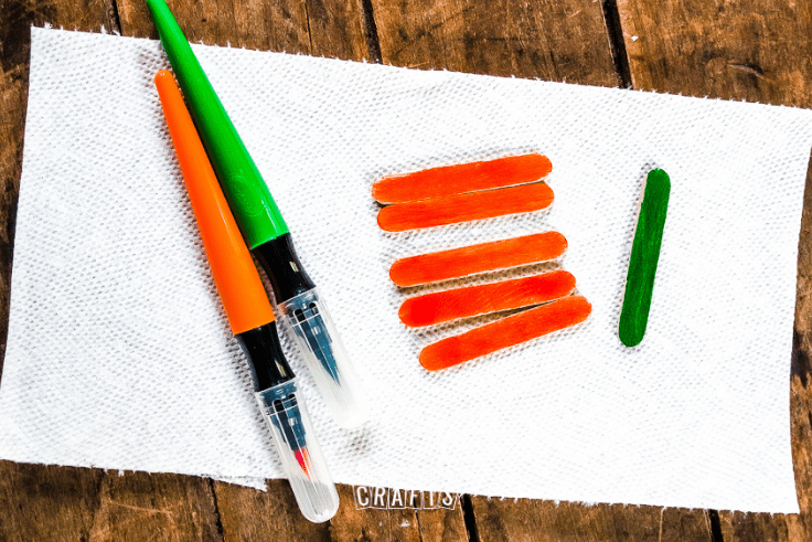 An orange paint pen, green paint pen, and painted popsicle sticks