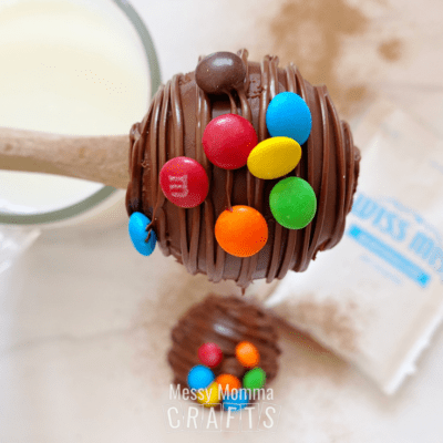 A spoon holding a hot cocoa bomb with M&Ms on the outside