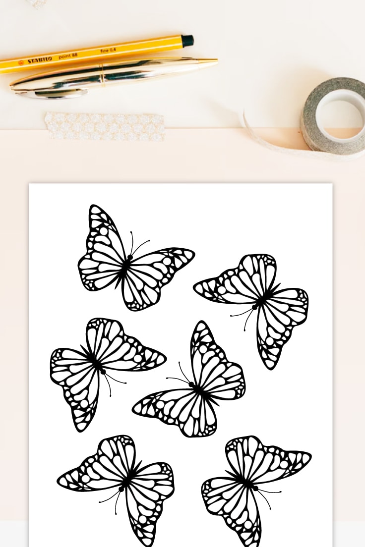 Preview of butterfly coloring page on white desk with pens, tape and paper underneath.