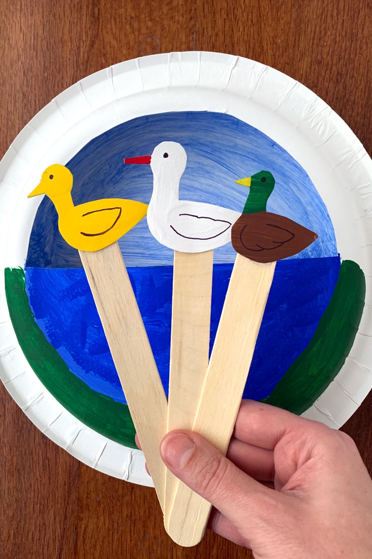 A yellow paper duck, white duck, and Mallard duck on craft sticks in front of a duck pond made from a round paper plate.
