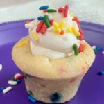 Funfetti Cookie Cup filled with Whipped Cream Cheese Filling and topped with sprinkles on a purple plate.