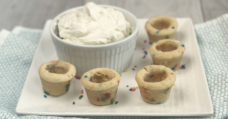 Cookie cups on a white plate with a bowl of whipped cream cheese filling.