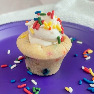 Funfetti Cookie Cup filled with Whipped Cream Cheese Filling and topped with sprinkles on a purple plate.