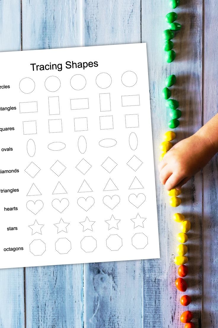Preview of tracing shapes kindergarten worksheet printable on wooden table with column of colorful candy on right side with kid hand taking a yellow candy. 