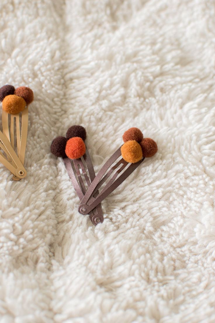 Two brown hair clips embellished with pompoms, sitting on a faux-fur blanket.