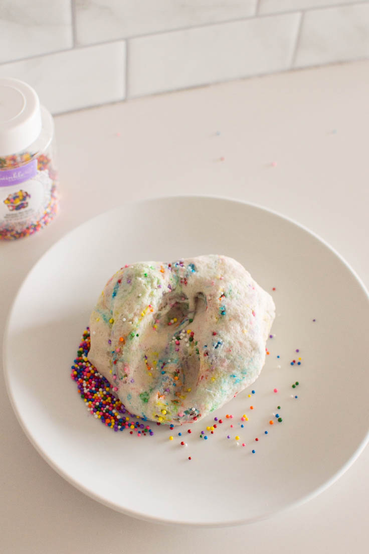 Bird's eye view of sprinkle play dough, sitting on a small white plate and surrounded by sprinkles