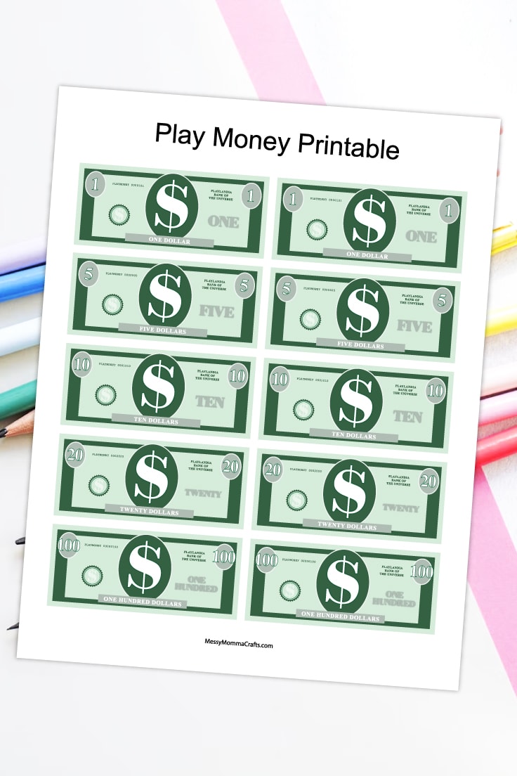 Preview of printable money PDF page on top of white desk with pastel pencils in the background view.