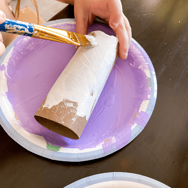 Child painting a toilet paper roll white.