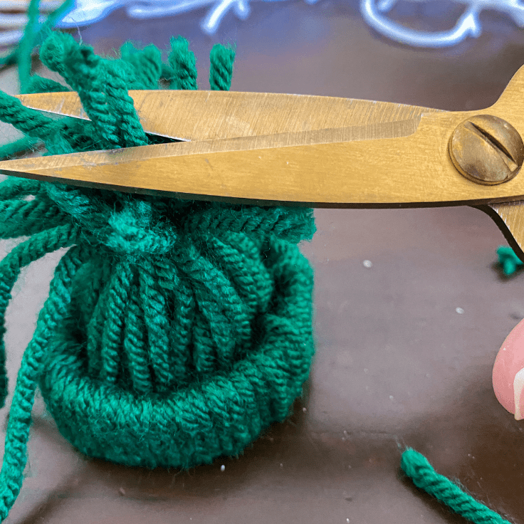 gold scissors cutting green yarn off the hat