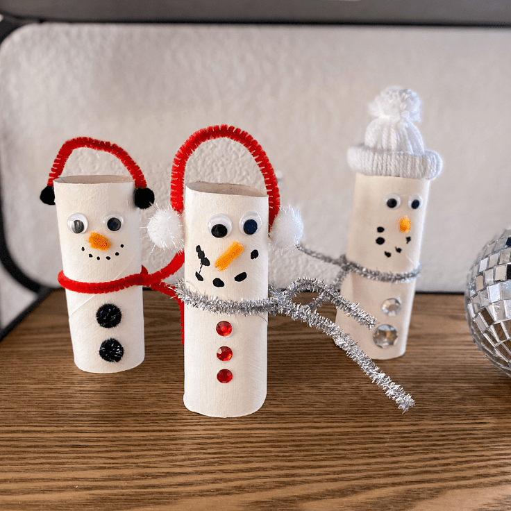 3 toilet paper snowmen, one with a scarf, two with ear muffs.