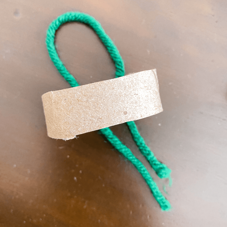 green yarn looped over a piece of toilet paper roll