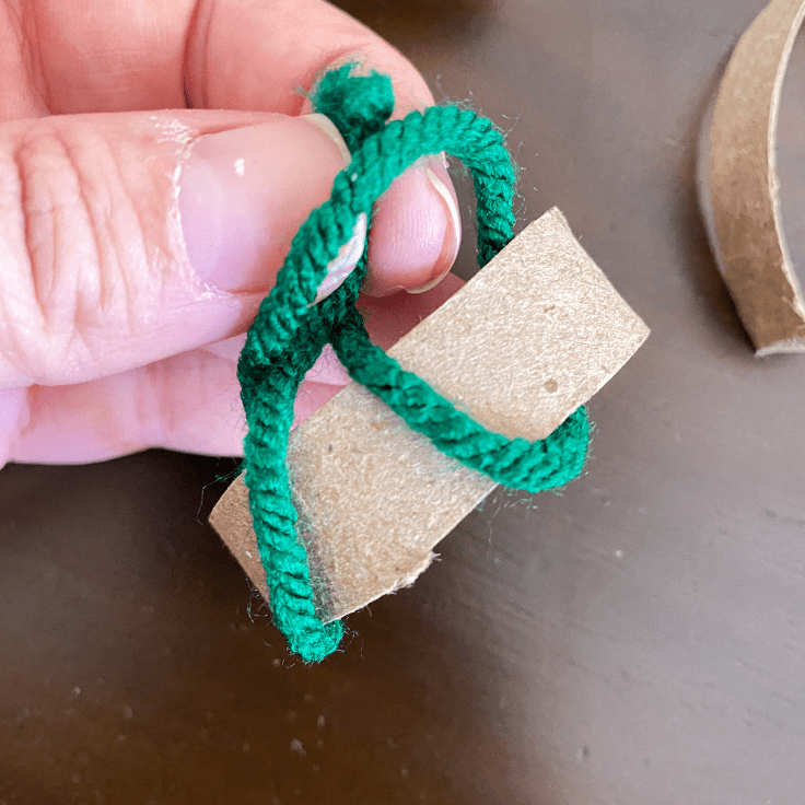 green yarn looped over a piece of toilet paper roll