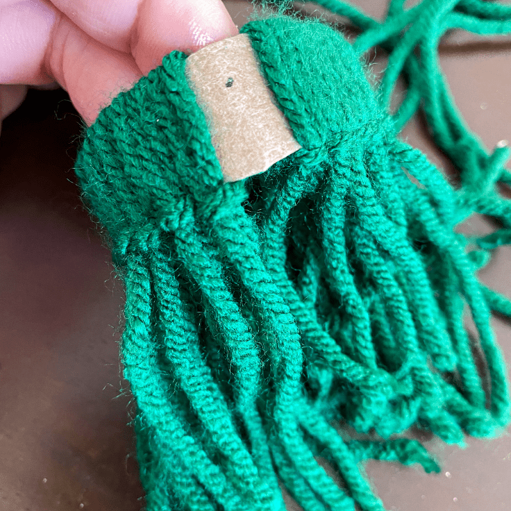 lots of green yarn looped and knotted over a toilet paper roll with a little bit of brown roll showing
