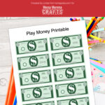 Preview of printable money PDF on top of desk with notebooks and jar of colored pencils.