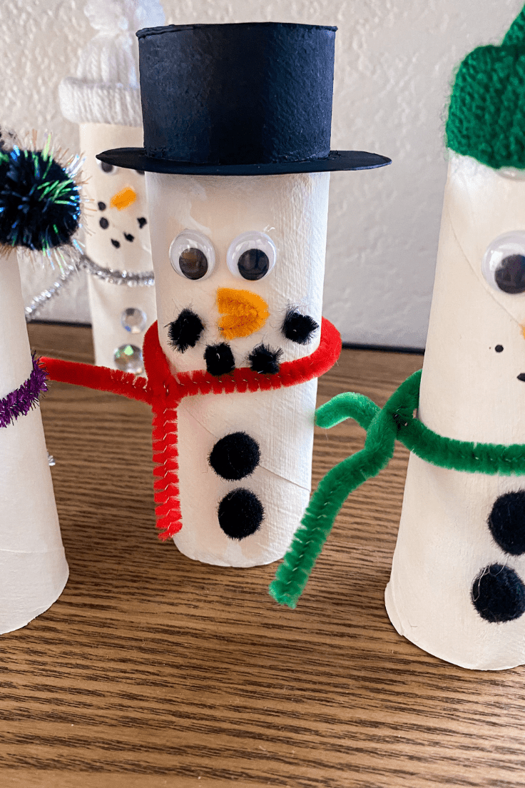 toilet paper snowman with a top hat, 3 snowman can be seen around it.