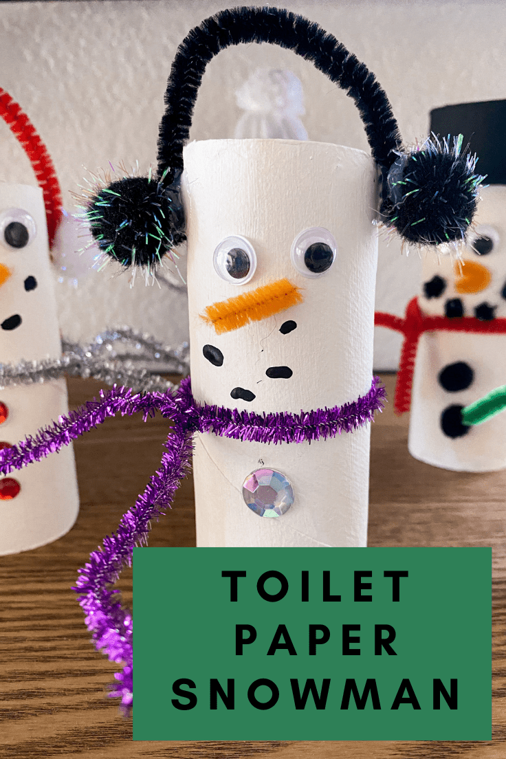 Toilet paper snowman with earmuffs, googley eyes, and a purple pipe cleaner scarf. 2 snowman can be seen in the background.