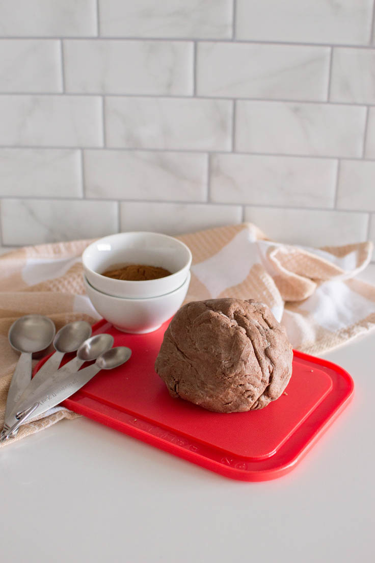 Homemade cinnamon playdough sitting on a red cutting board, surrounded by measuring spoons and a small bowl of ground cinnamon