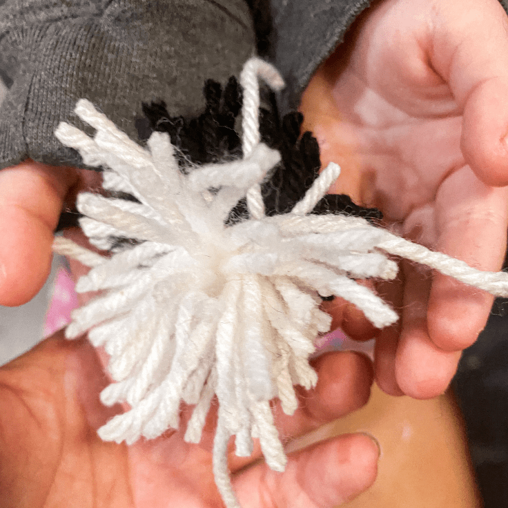 the start of a white and black pom pom being held in child's hands
