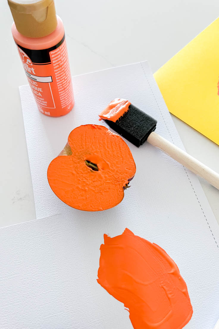 Half an apple coated with orange paint, sitting next to a foam brush