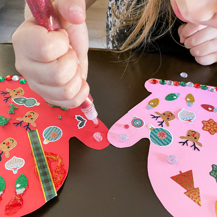 girl decorating paper mittens with red glitter glue