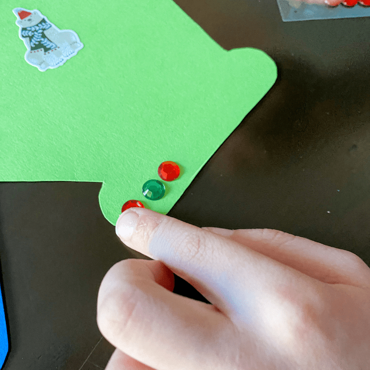 hand sticking gems on a green paper mitten
