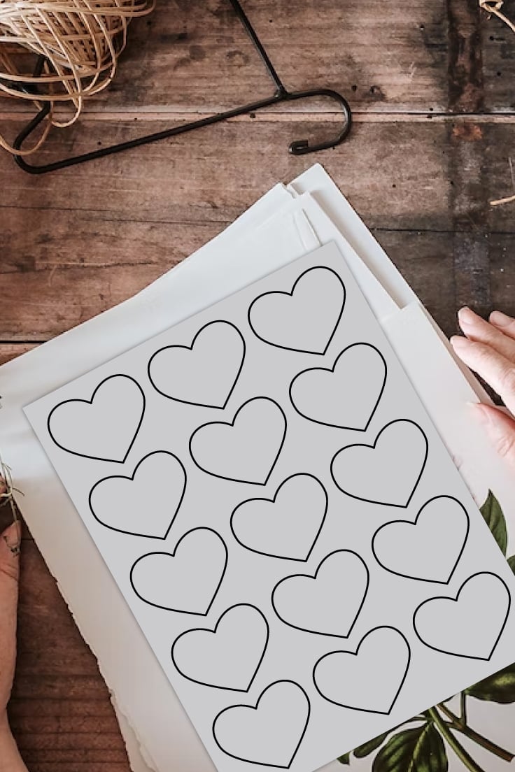Preview of printable heart template page on wooden desk on top of stack of papers with twine in upper left corner and woman's hands beside papers. 