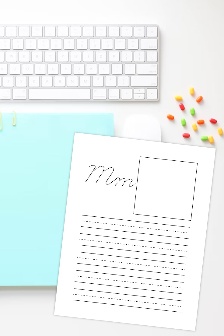 Preview of M cursive letter printable page on a white background with keyboard on top, light blue notebook and random colorful jellybeans on the right side.