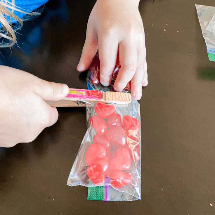 Child attaching a clothes pin to the center of a plastic bag filled with heart shaped jelly beans