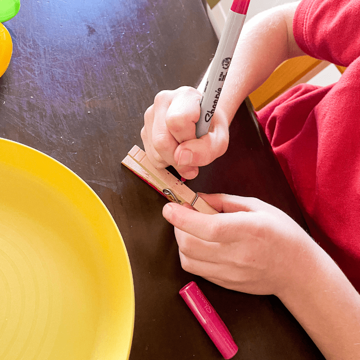 Child decorating a clothes pin with a red sharpie