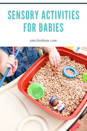 Baby reaching into a red bowl filled with cheerios and small toys