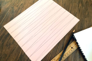 A piece of pink paper marked with lines to cut intro triangular strips.