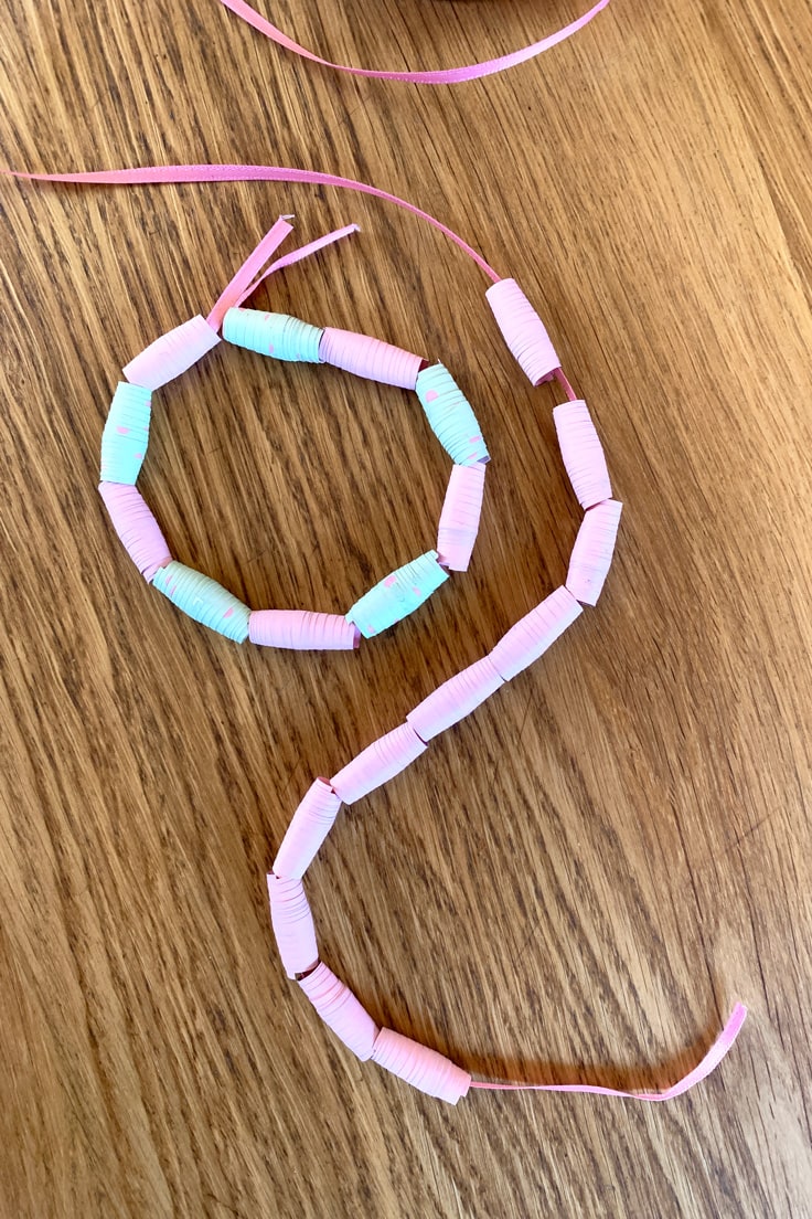 A ribbon strung with beads made from pink and green paper.