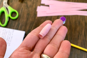 One pink paper bead in a hand with stack of paper strips in the background.