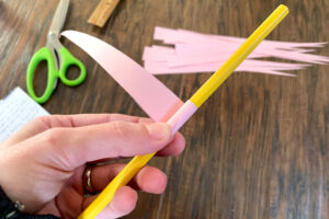 A pink paper triangle wrapping around a pencil to shape into a bead.