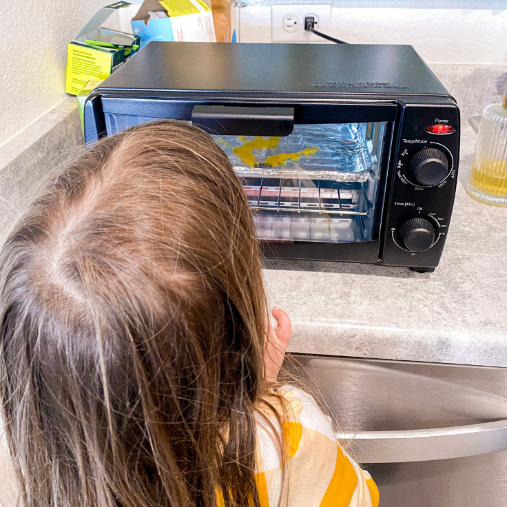 Child looking at a toaster oven that has a yellow shrinky dink handprint inside