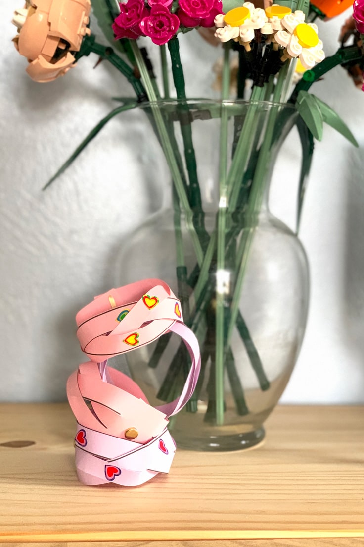 A stack of colorful paper bracelets beside a vase of plastic flowers.