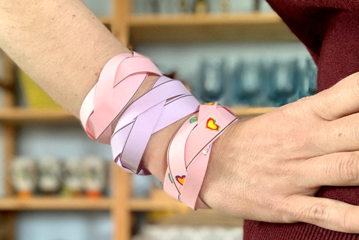 An arm wearing 3 pink and purple braided paper bracelets.