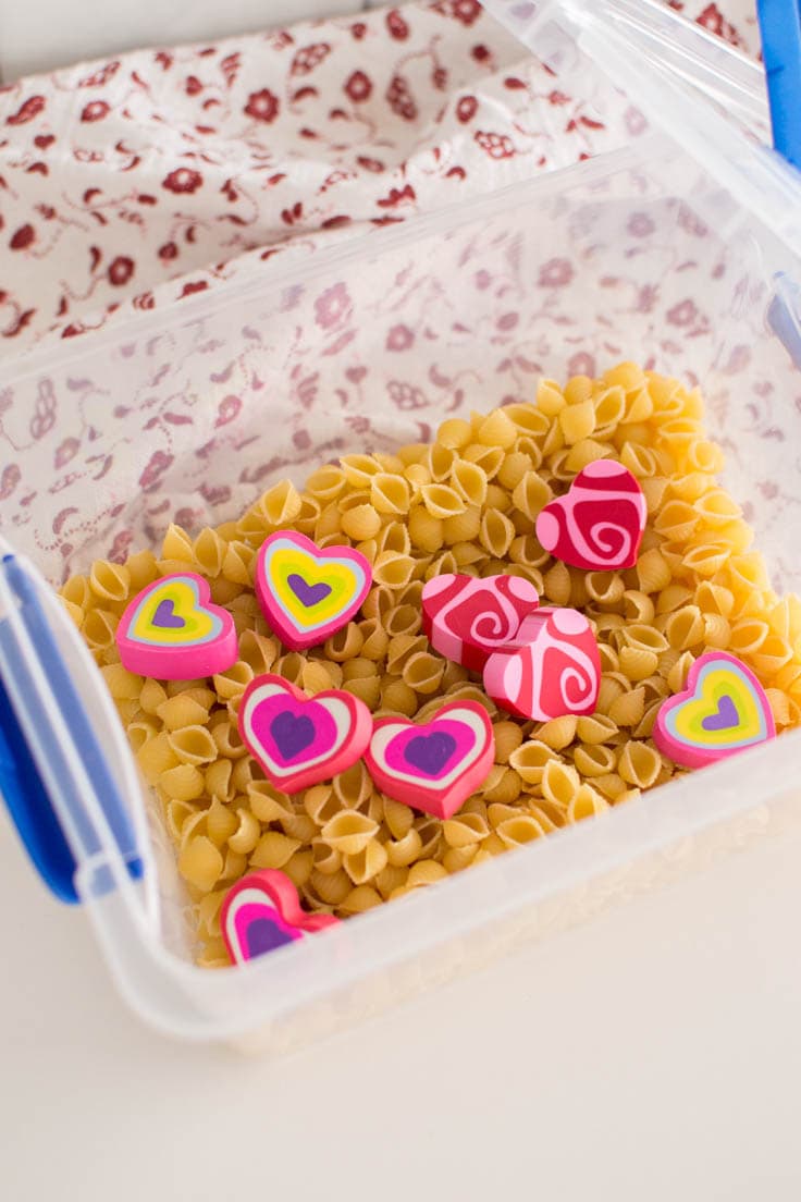 Adding heart-shaped erasers into a pasta-filled plastic bin