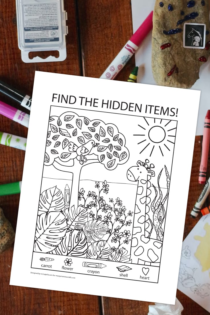 Preview of hidden pictures PDF printable with cute giraffe in landscape illustration and 5 hidden pictures to find, all above wooden desk with markers, crayons and paints.