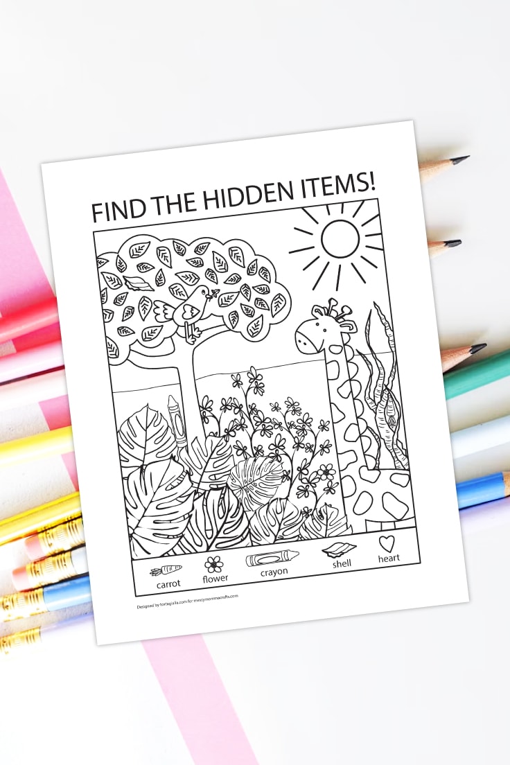 Preview of hidden pictures PDF printable with giraffe in landscape illustration and 5 hidden pictures to find, on top of white desk background with scattering of pencils in different colors under.