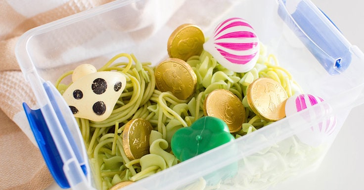 Close up view of a Green St. Patrick's Day Sensory Bin with cooked green pasta and a variety of small toys