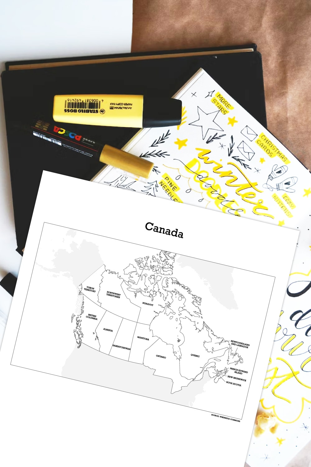 Preview of Canadian printable map on top of white desk with black notebook, kraft papers, highlighters, markers and open bullet journal underneath.  