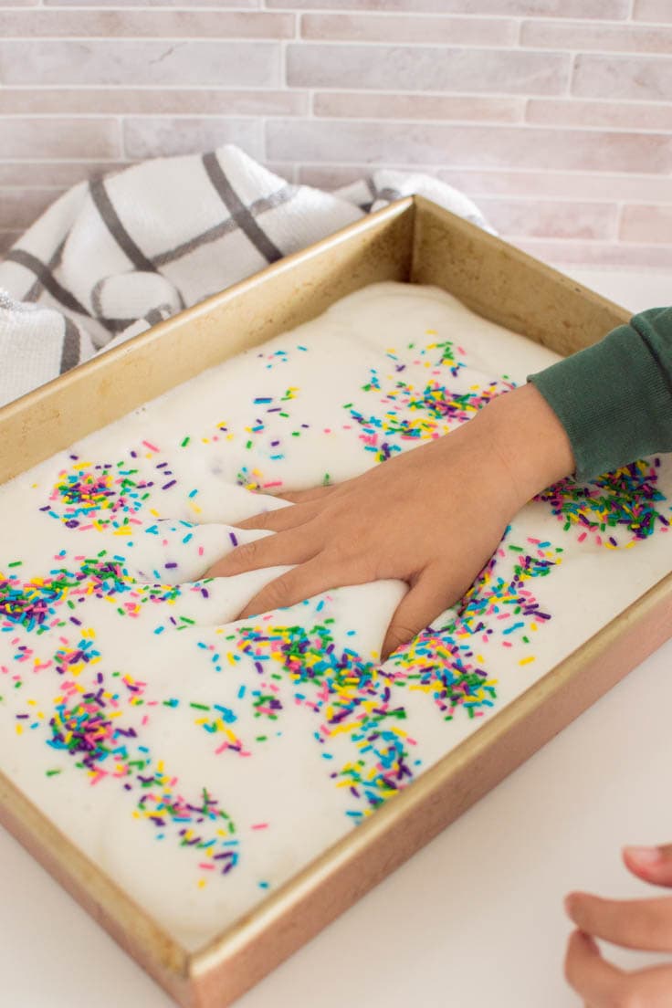 A hand digging into a sensory bin full of edible foam