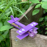 Purple popsicle stick airplane sitting in a garden.
