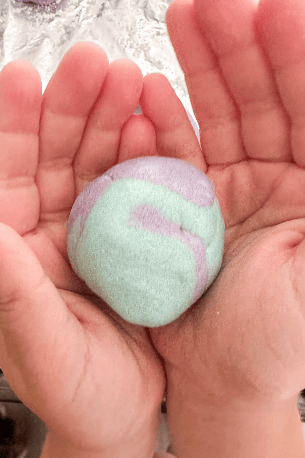 Hands holding a golf ball sized amount of two-toned purple and blue salt dough