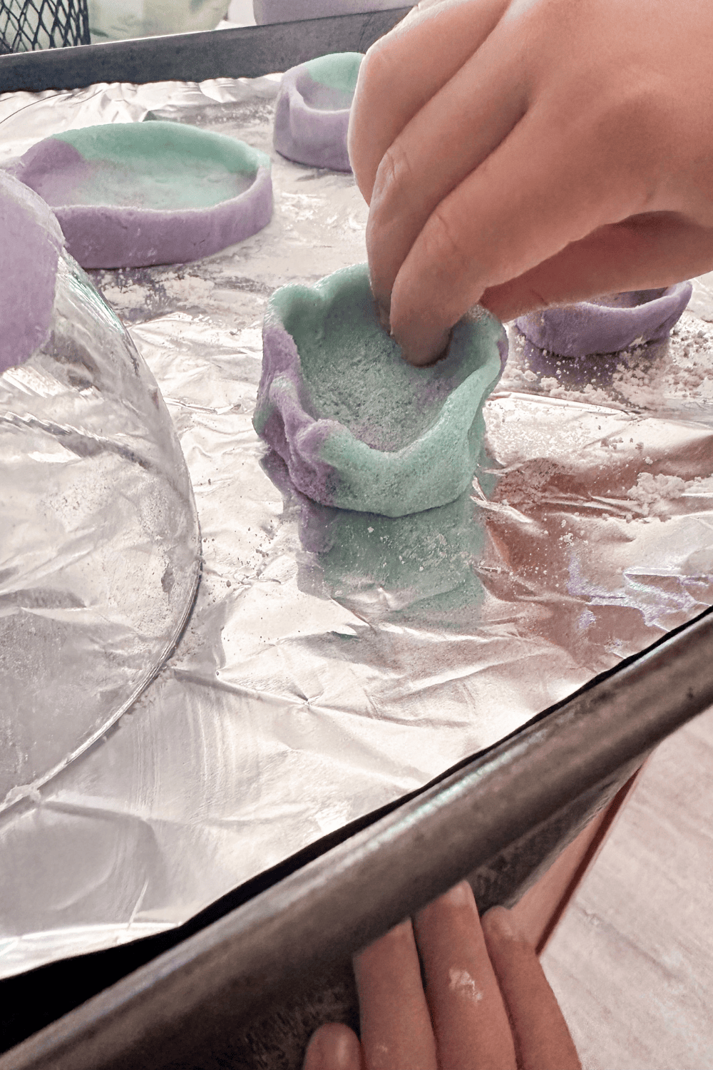 Child's hands pinching the edges of two-toned blue and purple salt dough to create a bowl