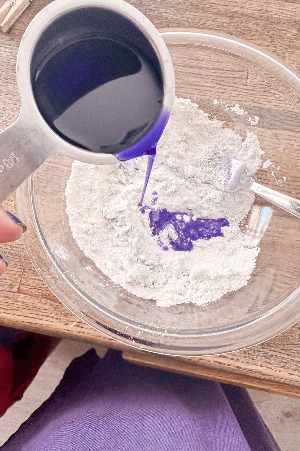 measuring cup pouring purple water into the flour and salt mixture