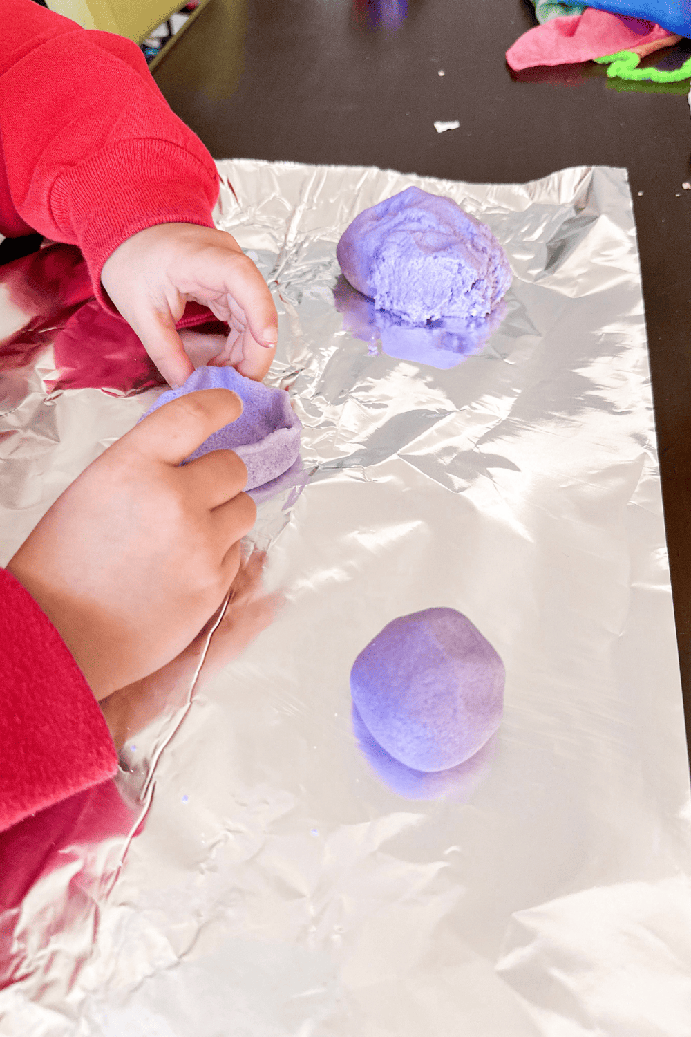 child pinching the edges of a purple salt dough bowl with purple salt dough laying in the background