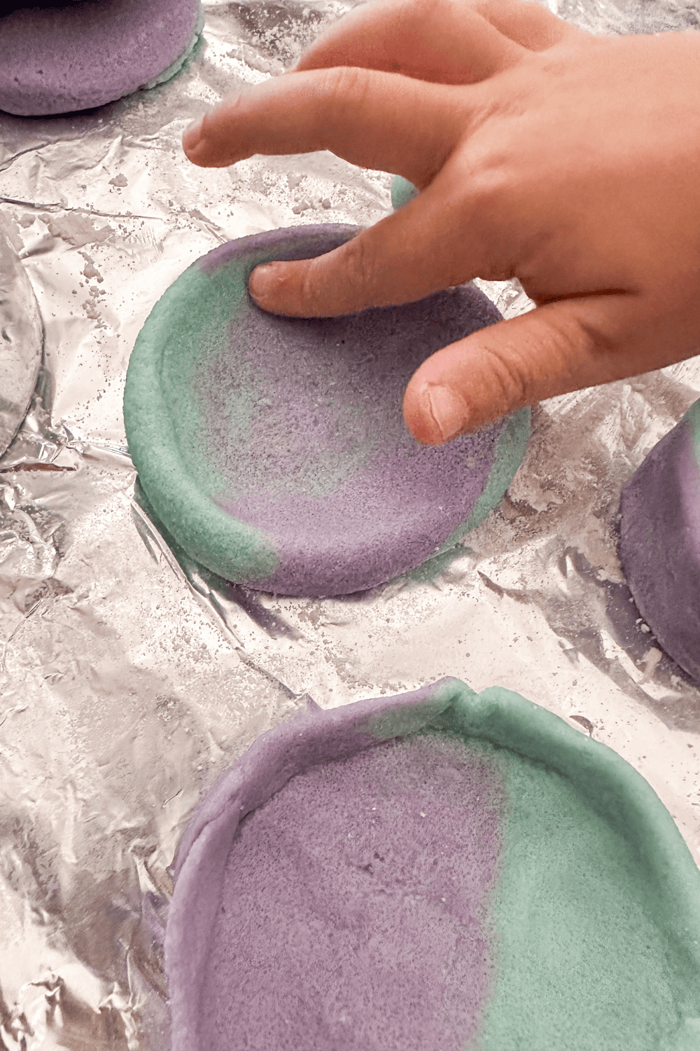 finger pushing out the center of a two-toned blue and purple marbled salt dough bowl